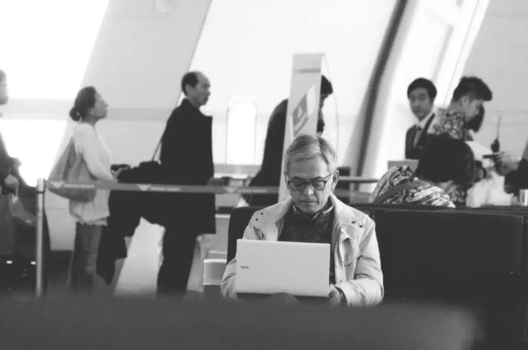 An old man using a laptop in the airport.